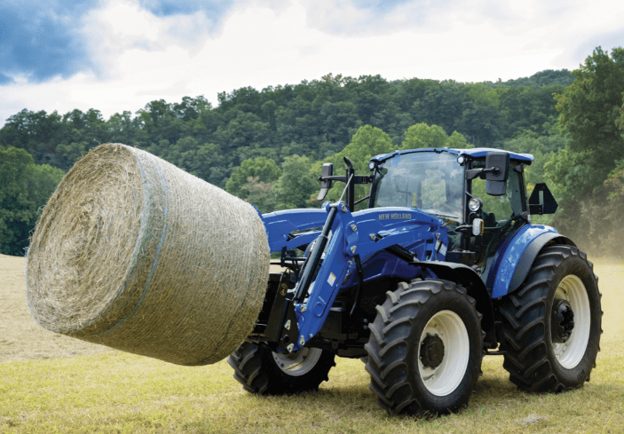 Tractor moving large hay bale with front attachment
