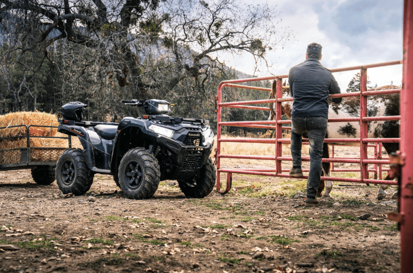 Man using ATV to haul a trailer of hay stacks to cows